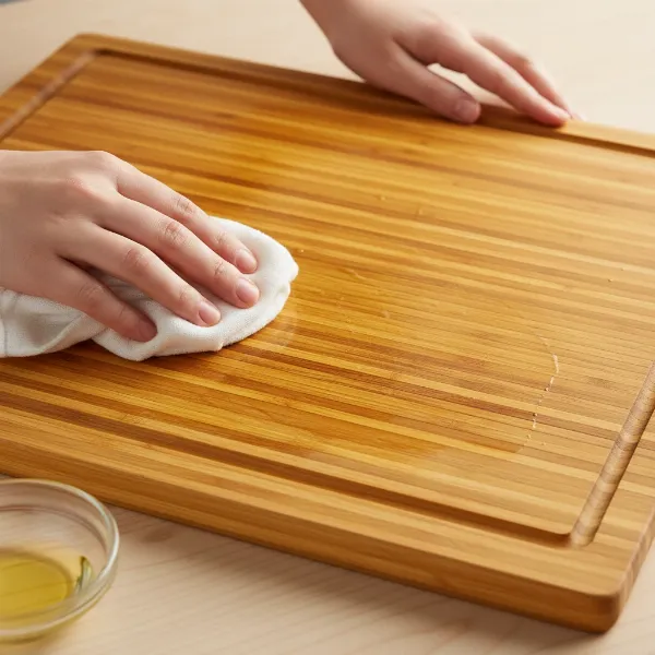 A person applying mineral oil to an HHXRISE Large Organic Bamboo Cutting Board, emphasizing proper maintenance.